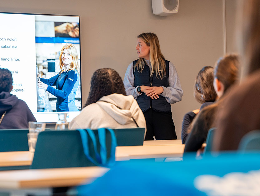 En kvinna står framför en presentation och undervisar åhörare 